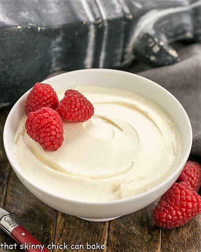 Homemade mascarpone cream in a white bowl garnished with raspberries.